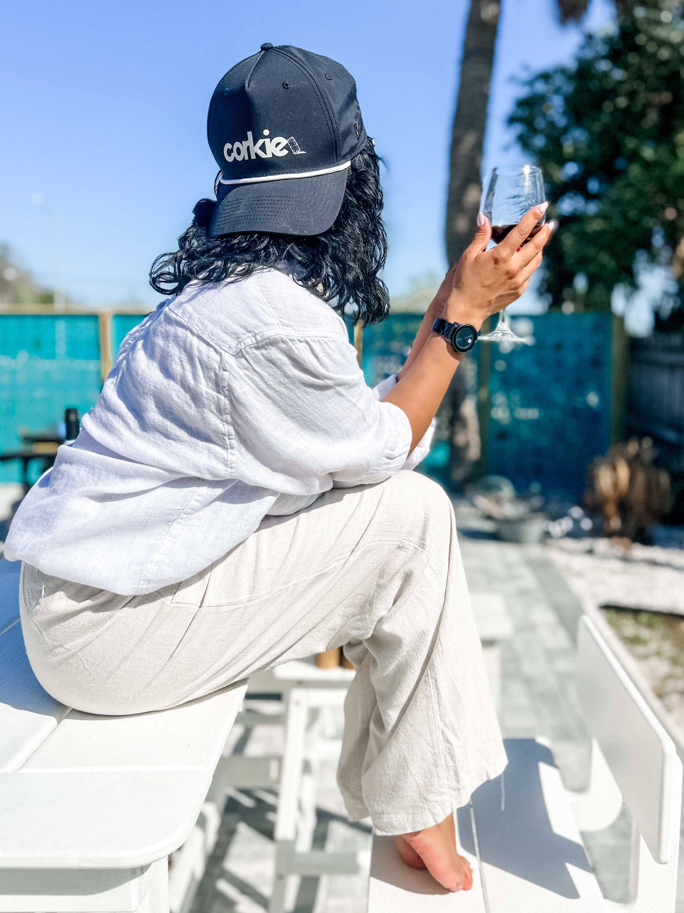 woman wearing a 'corkie' cap sitting outdoors with a wine.