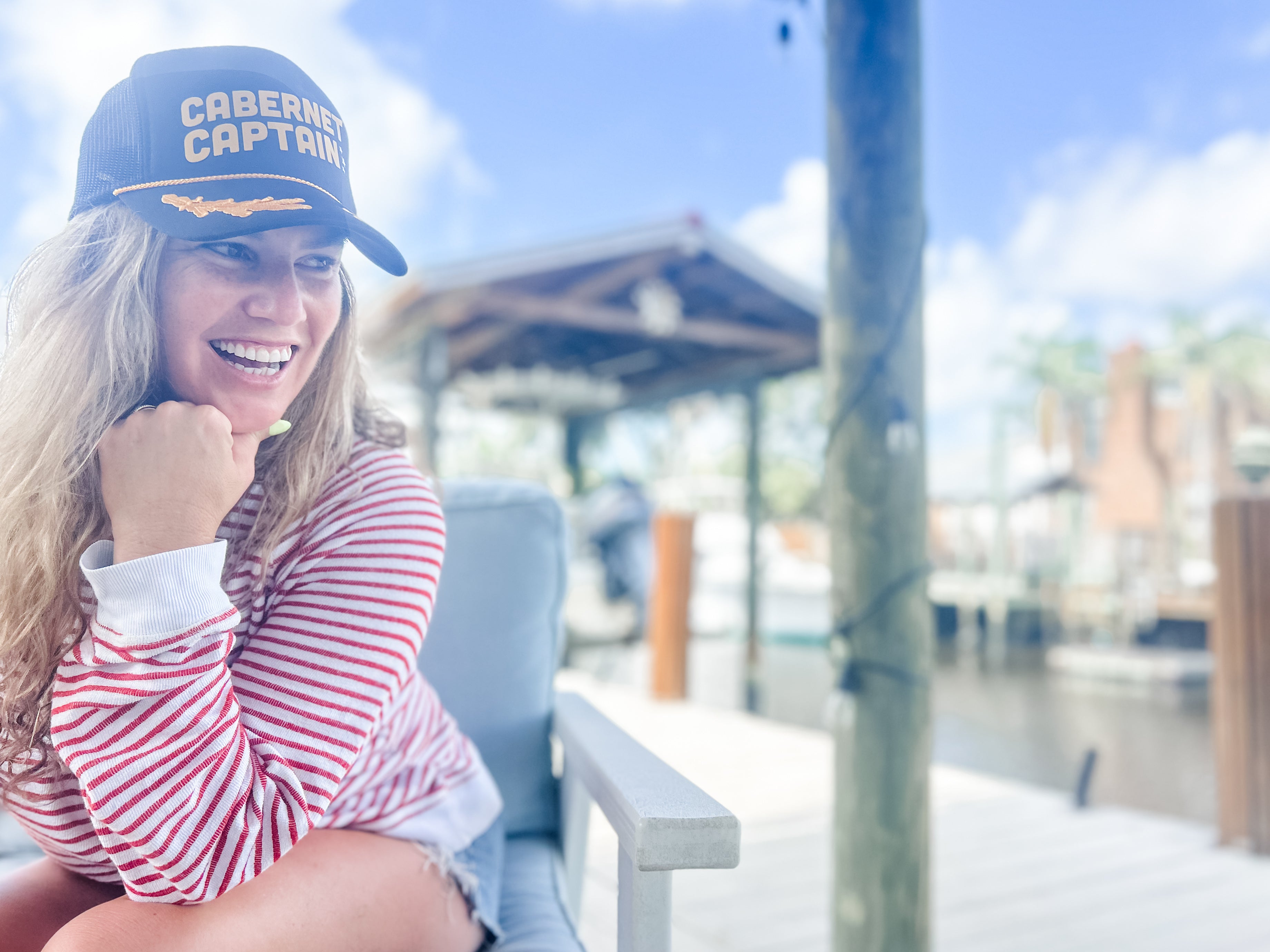 woman long hair sitting on dock with nautical Cabernet captain corkie wine apparel black trucker hat